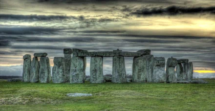 HD desktop wallpaper featuring Stonehenge, a man-made prehistoric monument with large standing stones under a dramatic, cloudy sky at sunset.