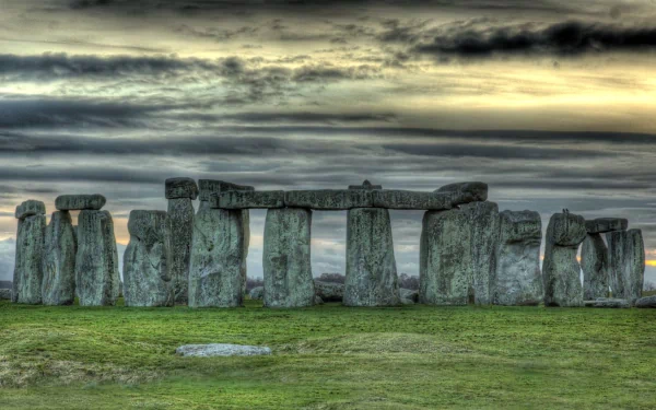 HD desktop wallpaper featuring Stonehenge, a man-made prehistoric monument with large standing stones under a dramatic, cloudy sky at sunset.