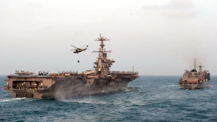 HD desktop wallpaper featuring the USS John C. Stennis (CVN-74) aircraft carrier in military operation with a helicopter flying above the ship on the open sea.