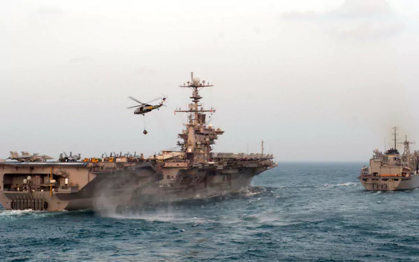 HD desktop wallpaper featuring the USS John C. Stennis (CVN-74) aircraft carrier in military operation with a helicopter flying above the ship on the open sea.