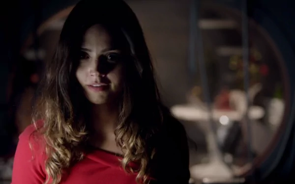 Clara Oswald, portrayed by Jenna Coleman, stands in a dimly lit scene from the TV show Doctor Who (2005), showcasing her unique character in a striking red outfit.