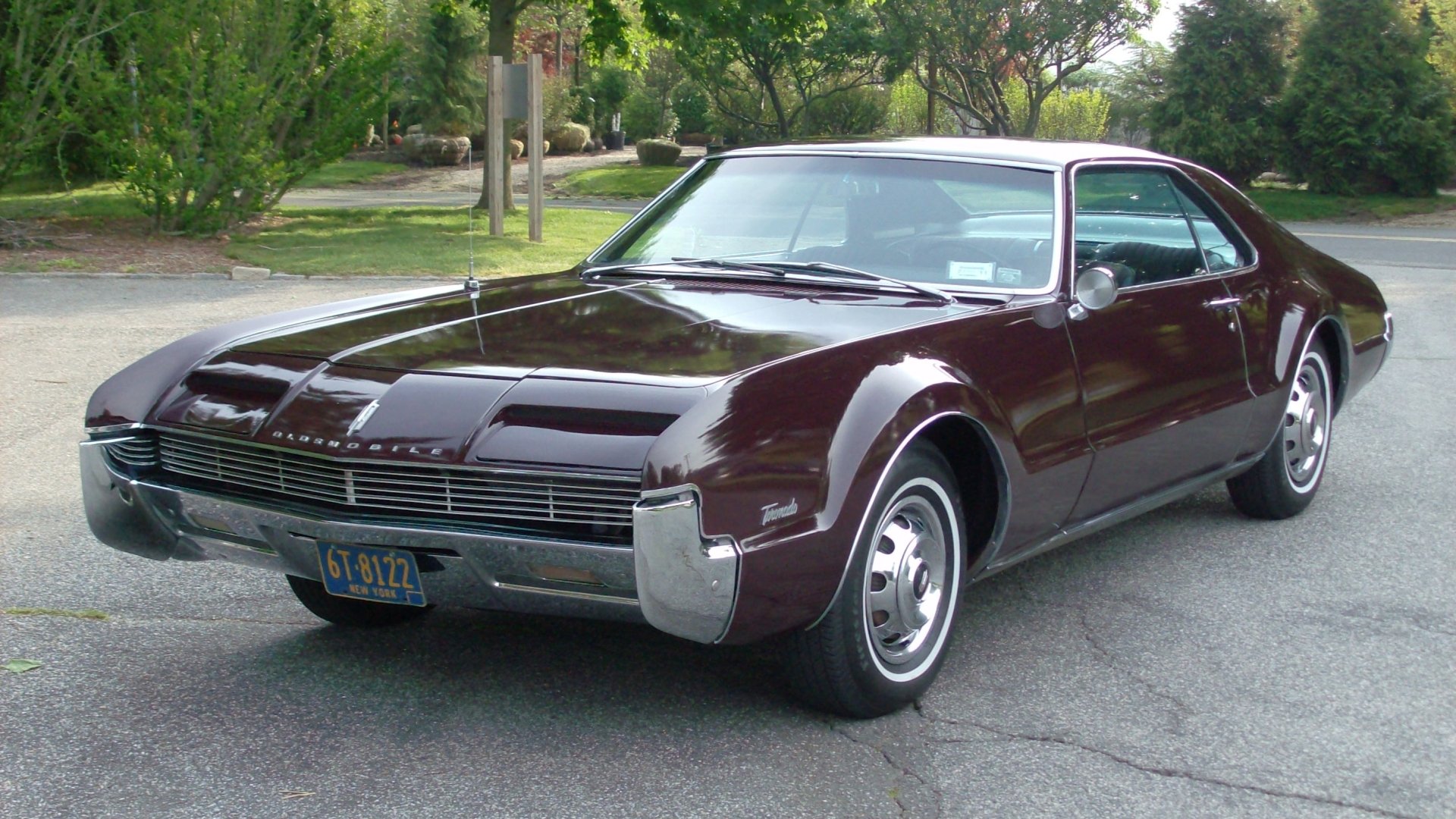 Maroon classic Oldsmobile Toronado parked on a suburban street, three-quarter front view with chrome bumpers and glossy finish — HD PC desktop wallpaper/background.