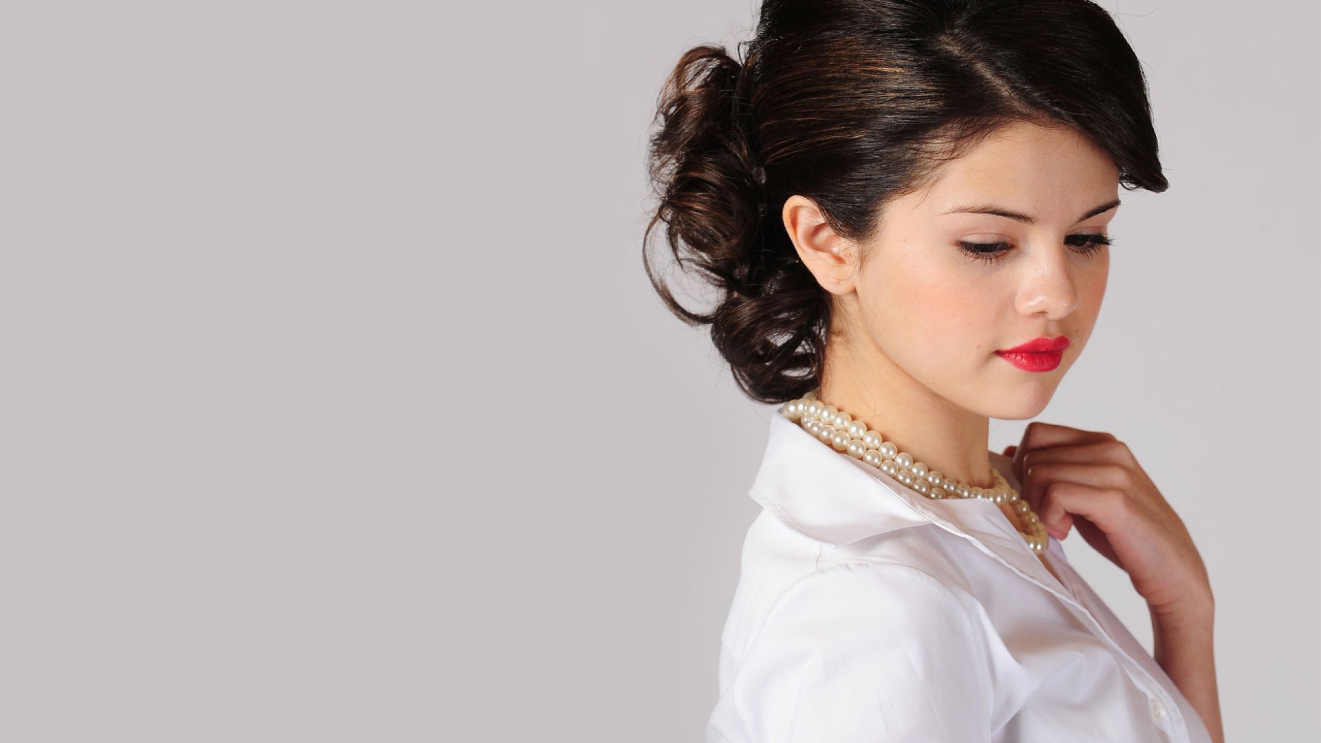 A stunning HD desktop wallpaper featuring Selena Gomez, showcasing her elegant profile with softly styled hair and a pearl necklace against a neutral background.
