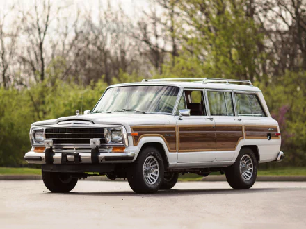 HD PC desktop wallpaper featuring a classic Jeep Grand Wagoneer with wood paneling parked on a paved surface, surrounded by trees in the background.