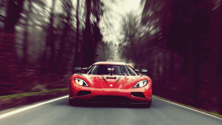 A captivating HD desktop wallpaper of a red Koenigsegg Agera, captured speeding down a forest road, with blurred trees enhancing the sense of motion.