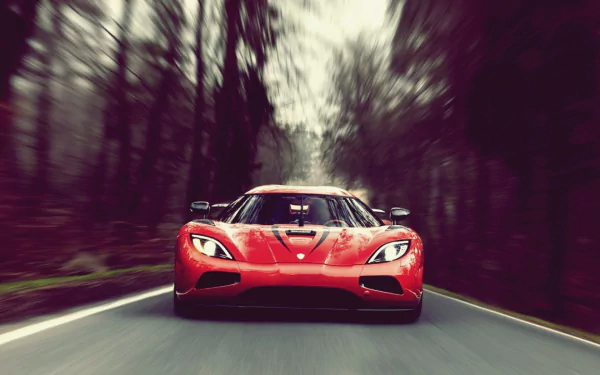 A captivating HD desktop wallpaper of a red Koenigsegg Agera, captured speeding down a forest road, with blurred trees enhancing the sense of motion.