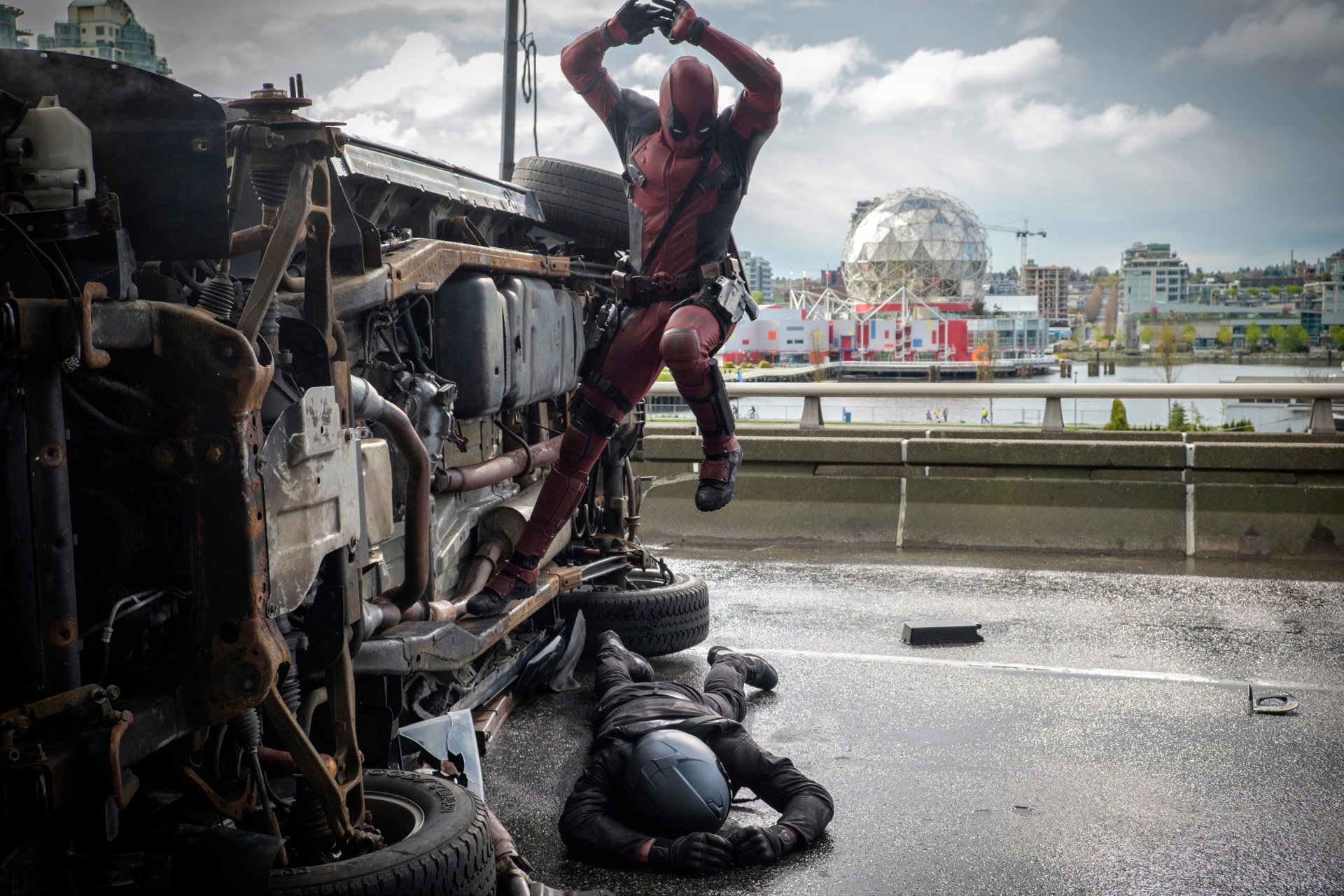 Deadpool leaps from an overturned vehicle, striking a foe on the ground in this dynamic HD desktop wallpaper from the movie Deadpool. Action-packed and visually striking.
