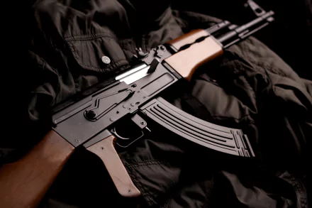 An HD wallpaper featuring an AK-47 resting on a dark, textured fabric, showcasing the weapon's striking details against a rich background.