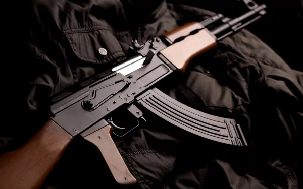 An HD wallpaper featuring an AK-47 resting on a dark, textured fabric, showcasing the weapon's striking details against a rich background.