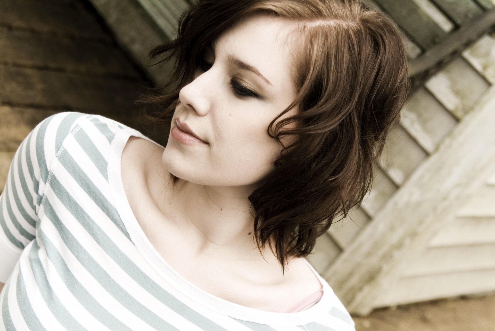 A woman with short, wavy hair in a striped shirt gazes thoughtfully to the side, set against a rustic wooden background, making for an inspiring HD desktop wallpaper.