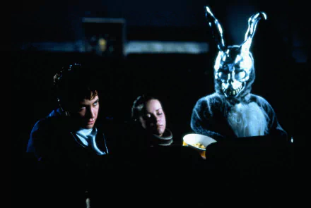 HD desktop wallpaper featuring Jake Gyllenhaal and Jena Malone in a dark scene from the movie Donnie Darko, with the iconic eerie rabbit figure in the background.