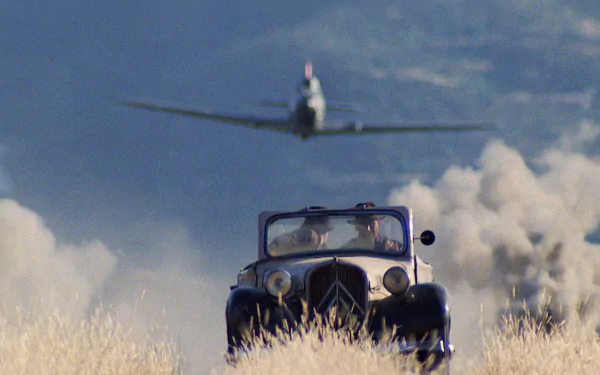 HD PC desktop wallpaper from the movie Indiana Jones and the Last Crusade, featuring a vintage car chased by a low-flying plane over a dusty field.