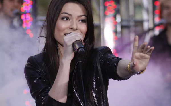 Female celebrity singing into a microphone on a smoky, colorful stage, reaching toward the audience — 2K Quad HD PC desktop wallpaper background.