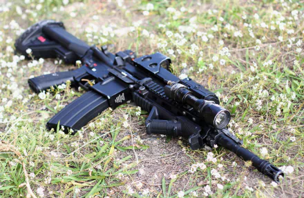 HD desktop wallpaper featuring a Heckler & Koch HK416 rifle resting on grassy terrain, highlighting its tactical design and details in a crisp, man-made setting.