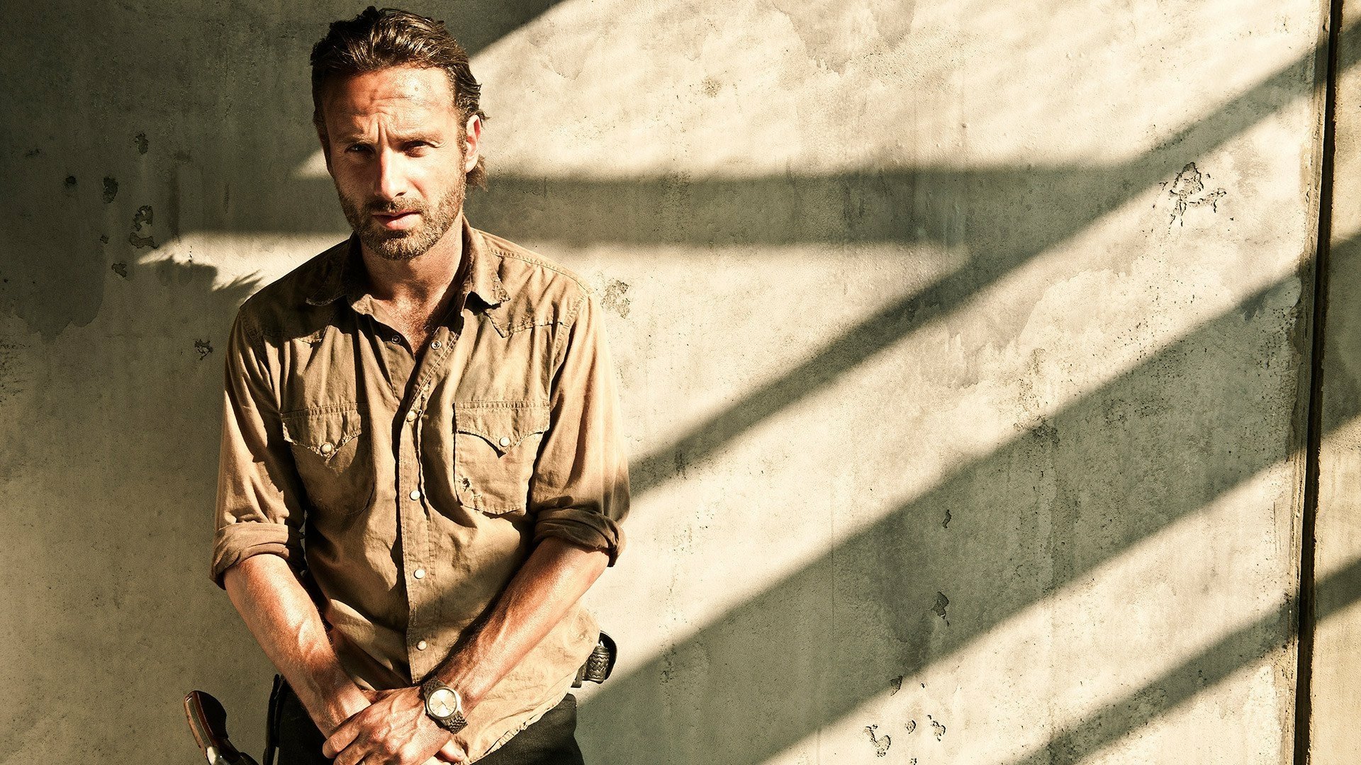Rick Grimes, portrayed by Andrew Lincoln, stands pensively against a textured wall, bathed in shafts of light, in this HD wallpaper from The Walking Dead.