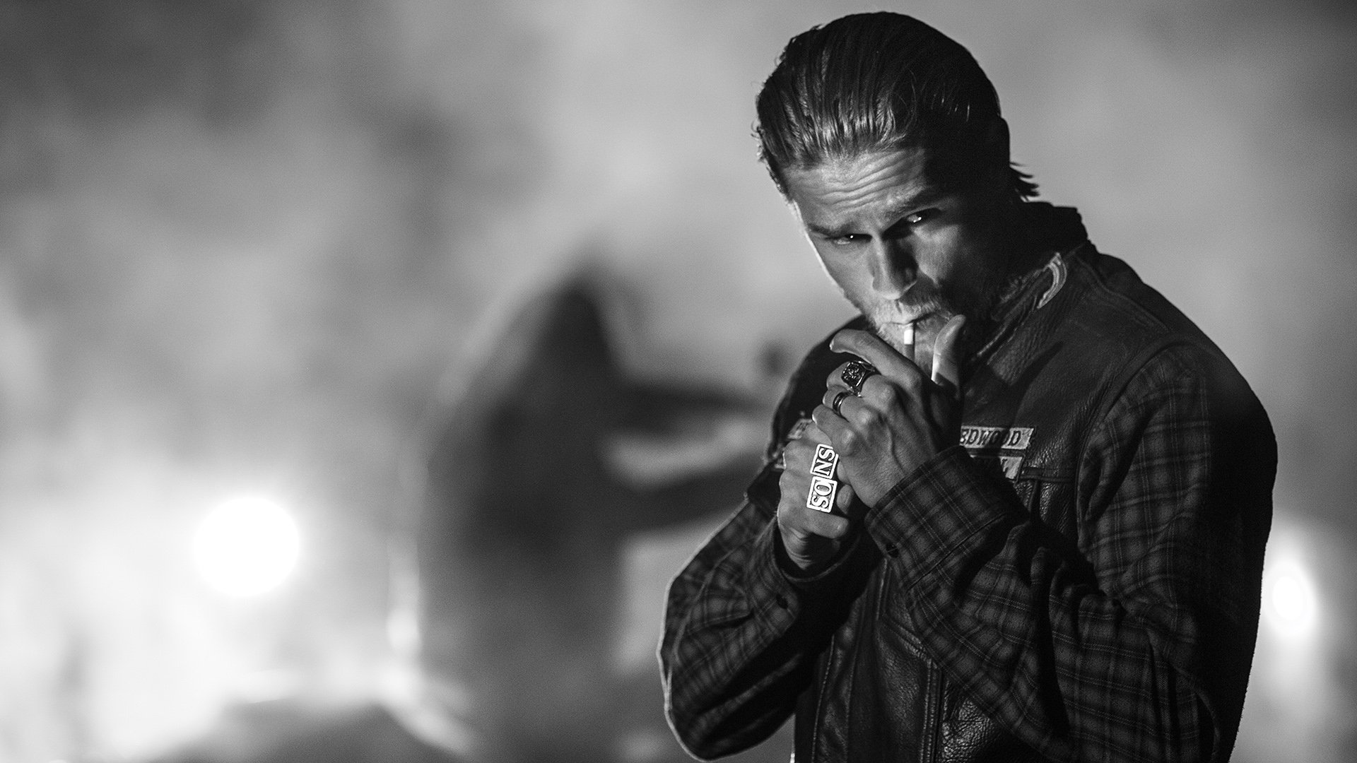 Black-and-white HD desktop wallpaper featuring a brooding character from the TV show Sons of Anarchy, lighting a cigarette with a smoky, intense background.