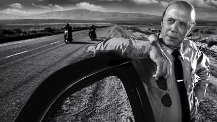 Black and white HD desktop wallpaper from the TV show Sons of Anarchy, featuring a man leaning on a car door with two motorcyclists riding on a long deserted road.