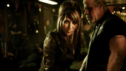 HD PC desktop wallpaper for the TV show Sons of Anarchy: two leather-clad club members in a dim, smoky bar — a woman staring intently at the viewer with a man standing beside her.