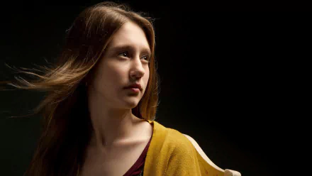 A striking HD wallpaper featuring Taissa Farmiga, known for her role in the TV show American Horror Story, captured in a thoughtful pose against a dark background.