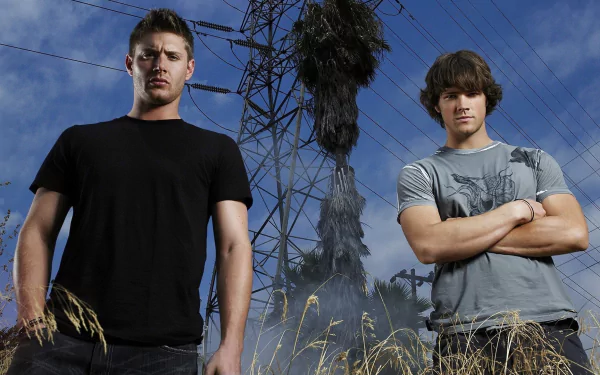 HD wallpaper featuring characters from the TV show Supernatural, standing confidently in front of a power line against a dramatic sky.