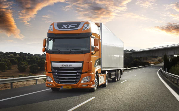 HD desktop wallpaper featuring a bright orange DAF XF truck driving on a highway under a partly cloudy sky during sunrise or sunset.