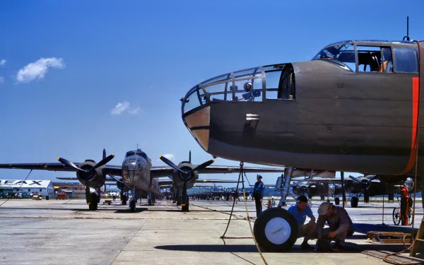 HD PC desktop wallpaper showing a military North American B-25 Mitchell bomber on the tarmac with crew members performing maintenance under clear blue skies.