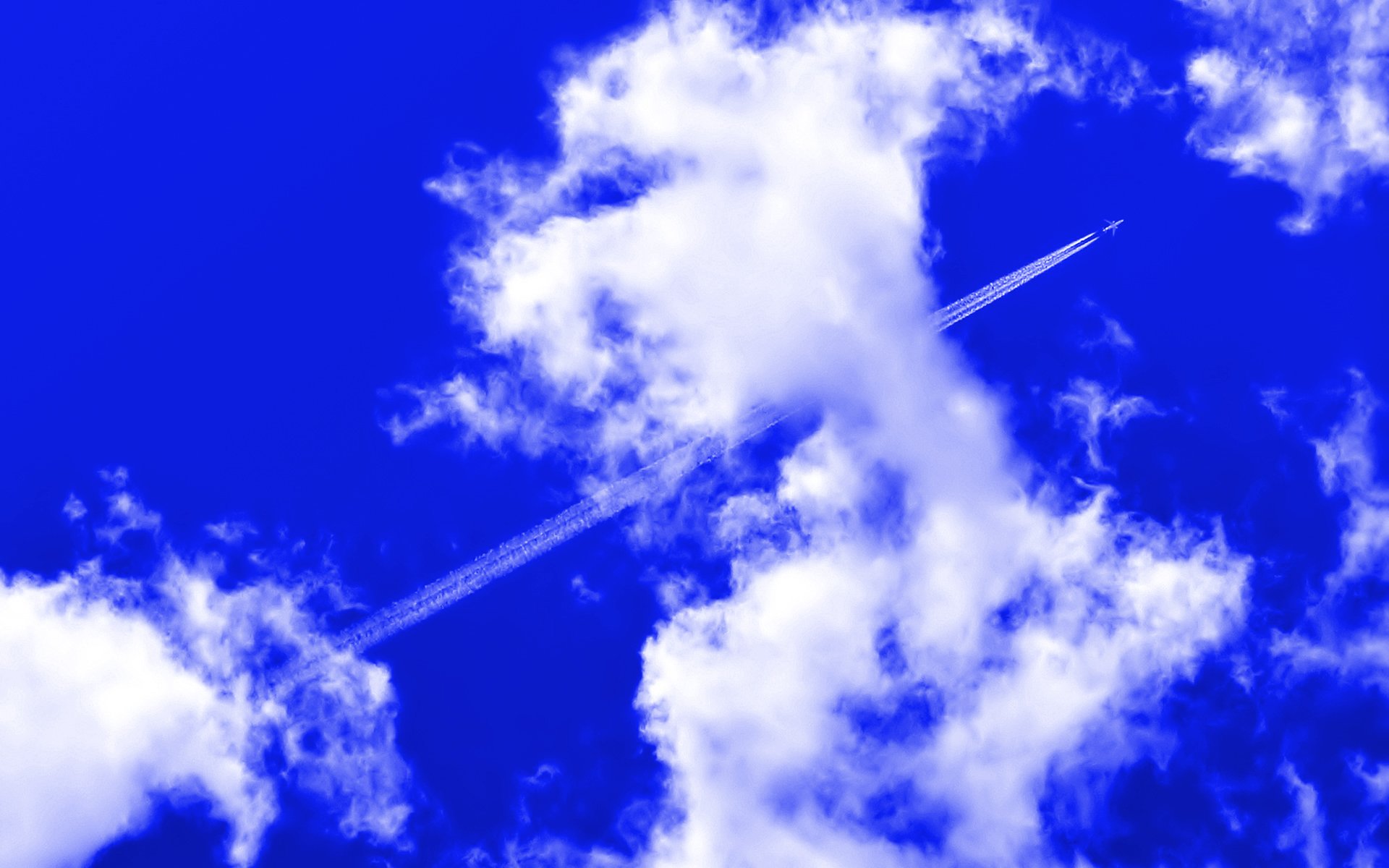 A jet leaves a contrail through a clear blue sky dotted with puffy white clouds, captured in a high-definition nature wallpaper.