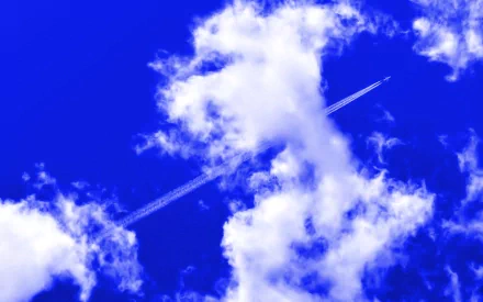 A jet leaves a contrail through a clear blue sky dotted with puffy white clouds, captured in a high-definition nature wallpaper.