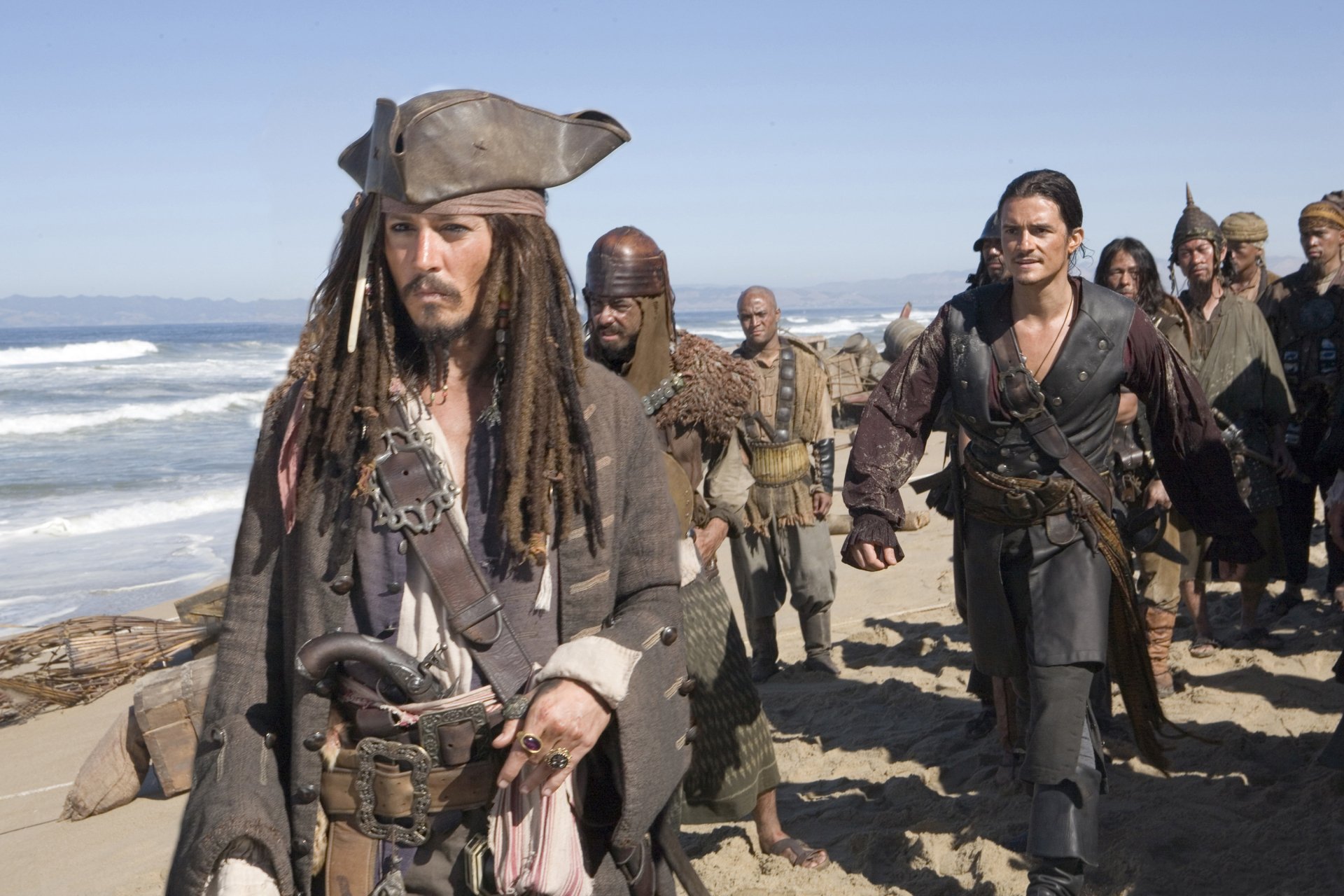 HD desktop wallpaper from Pirates of the Caribbean: At World's End featuring Jack Sparrow (Johnny Depp) and Will Turner (Orlando Bloom) walking on a beach with a group behind them.