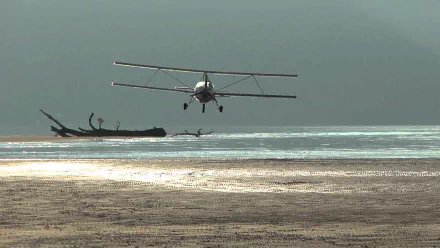 Aviasud Mistral biplane flying low over a sunlit beach and shallow sea, presented as an HD PC desktop wallpaper/background.