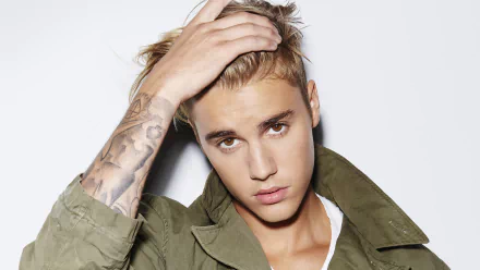 HD desktop wallpaper of Justin Bieber in a white shirt and green jacket, touching his hair, with a tattoo visible on his forearm. Background is plain white. Tags: music, Justin Bieber.