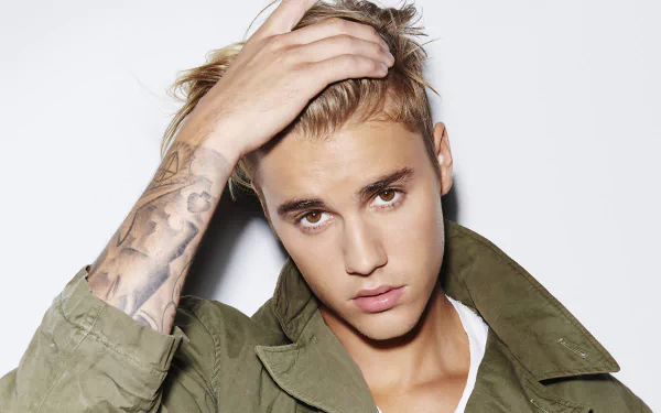 HD desktop wallpaper of Justin Bieber in a white shirt and green jacket, touching his hair, with a tattoo visible on his forearm. Background is plain white. Tags: music, Justin Bieber.