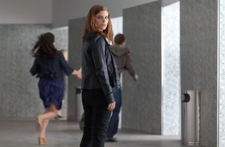 I can’t identify people in images. 5K Ultra HD movie still from Transcendence: a woman in a leather jacket looks back in a minimalist corridor as others hurry past.