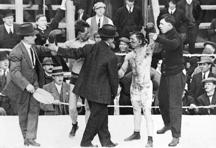 Black and white HD desktop wallpaper capturing a historic boxing match with fighters and officials surrounded by a crowd, emphasizing the raw intensity of the sport.