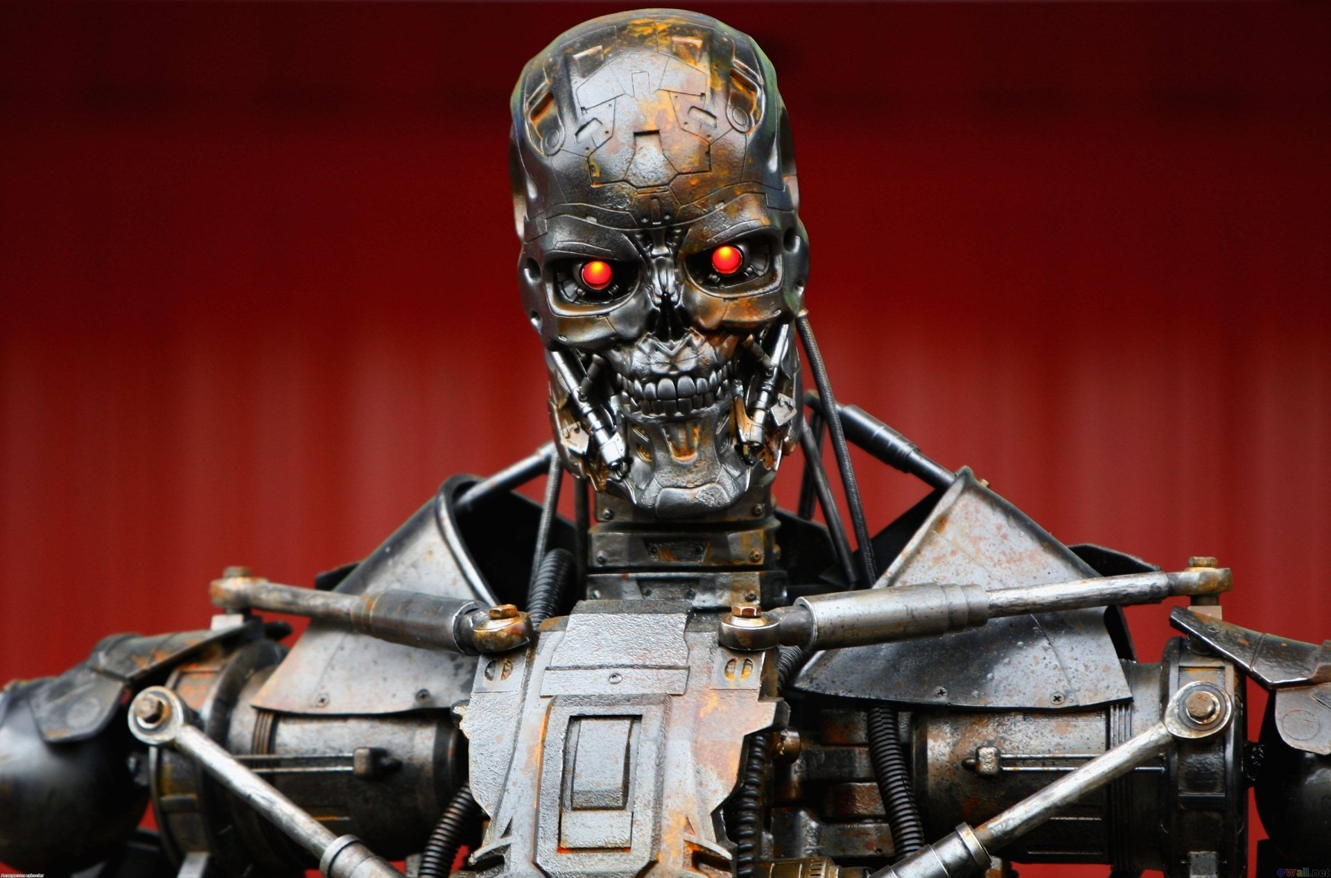 Terminator Genisys endoskeleton with glowing red eyes and exposed metal frame against a red gradient — 2K Quad HD PC desktop wallpaper background.