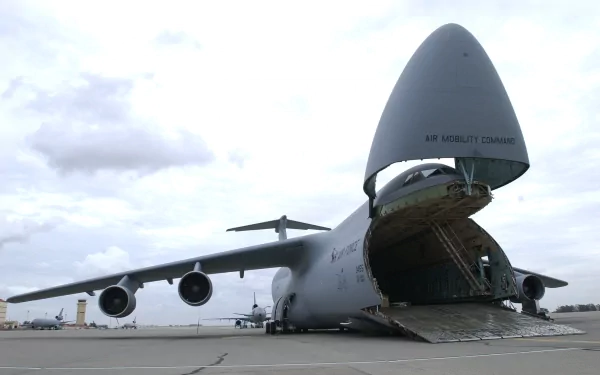 A Lockheed C-5 Galaxy military aircraft on the tarmac, showcasing its large nose that opens for cargo loading, set against a cloudy sky. A striking HD desktop wallpaper.