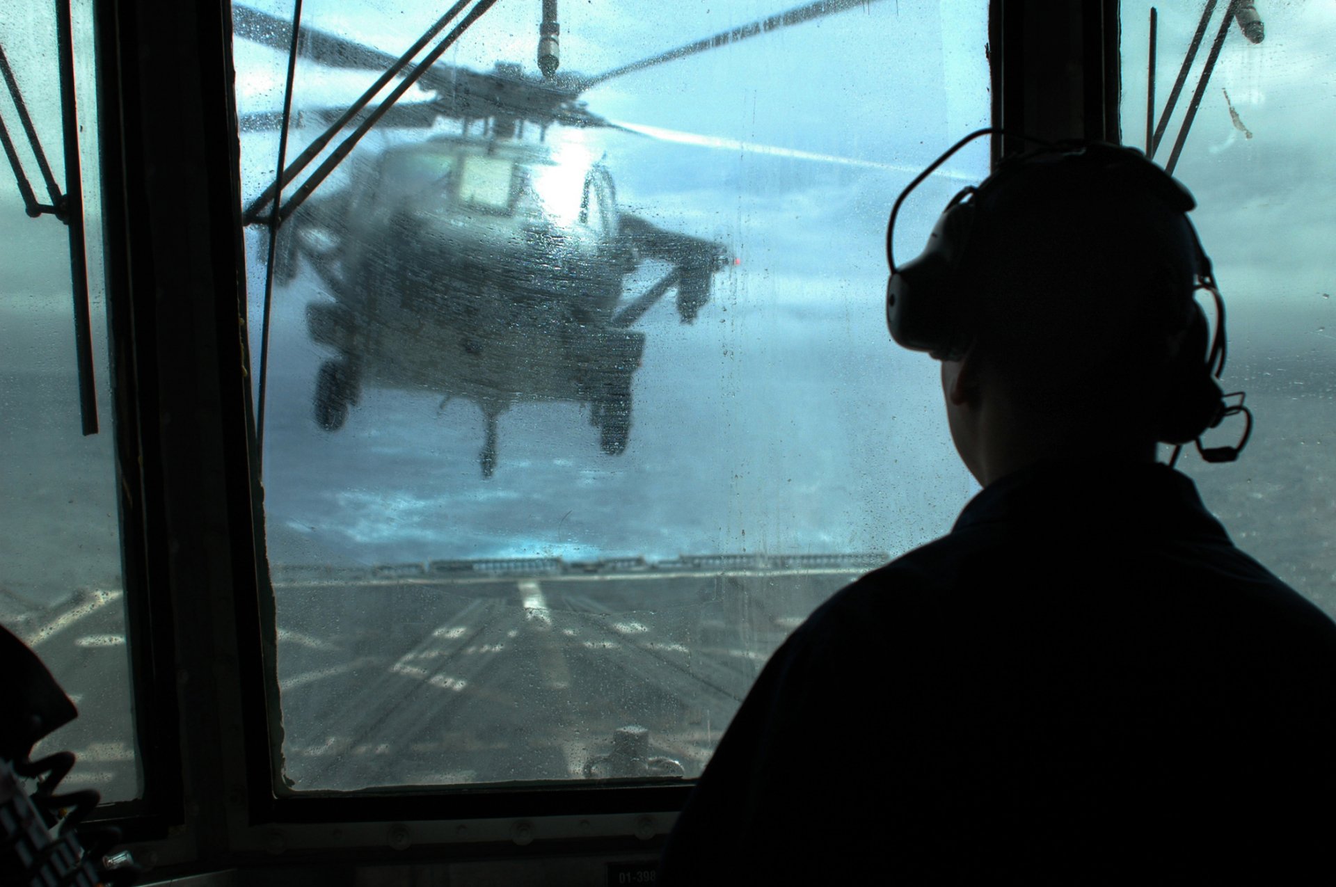 A military helicopter hovers in the sky, viewed from inside a control tower. The scene captures dynamic aerial operations, showcasing advanced technology in a striking HD background.