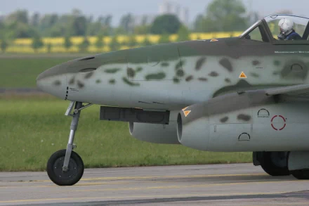 Close-up of a Messerschmitt Me 262, a military aircraft, showcasing its distinctive camouflage and design, set against a vibrant green landscape. HD desktop wallpaper.