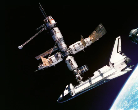 HD desktop wallpaper showing NASA’s Space Shuttle Atlantis docked with the Mir space station orbiting Earth in outer space.
