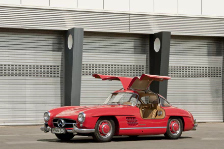 Red Mercedes-Benz 300SL vehicle with gullwing doors parked before industrial shutters — 5K Ultra HD PC desktop wallpaper/background.