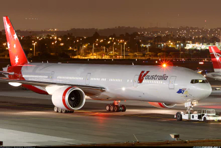 A stunning Boeing 777 aircraft, painted in vibrant Australia livery, is parked at an airport at night, illuminated by city lights, making a striking HD desktop wallpaper.