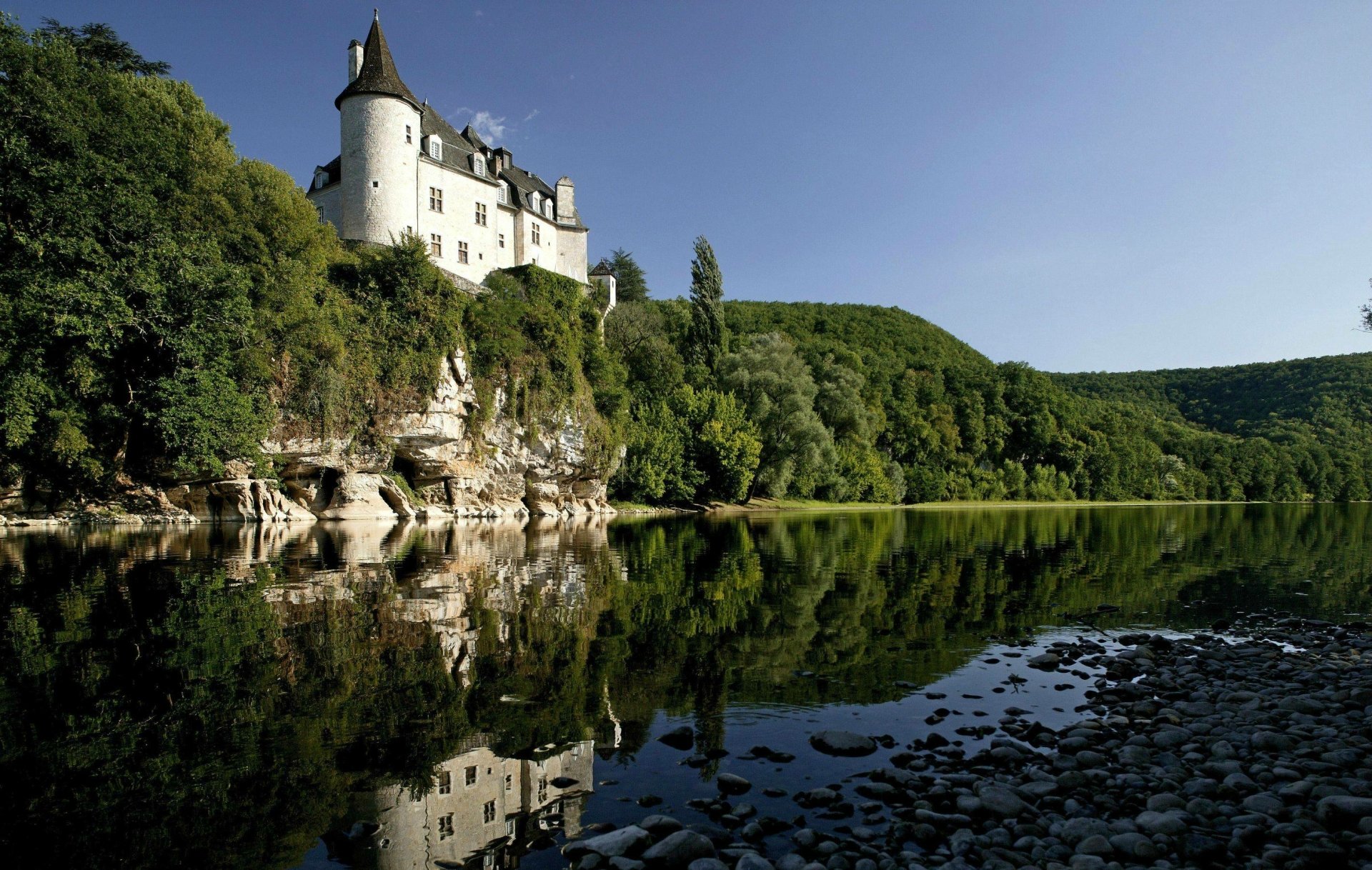 Chateau de la Treyne on cliffs above a reflective river, surrounded by green hills — 2K Quad HD man-made PC desktop wallpaper/background.