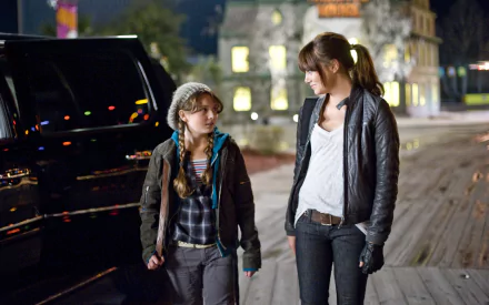 Abigail Breslin and Emma Stone share a moment in a scene from the movie Zombieland, set against a backdrop of a nighttime urban landscape.