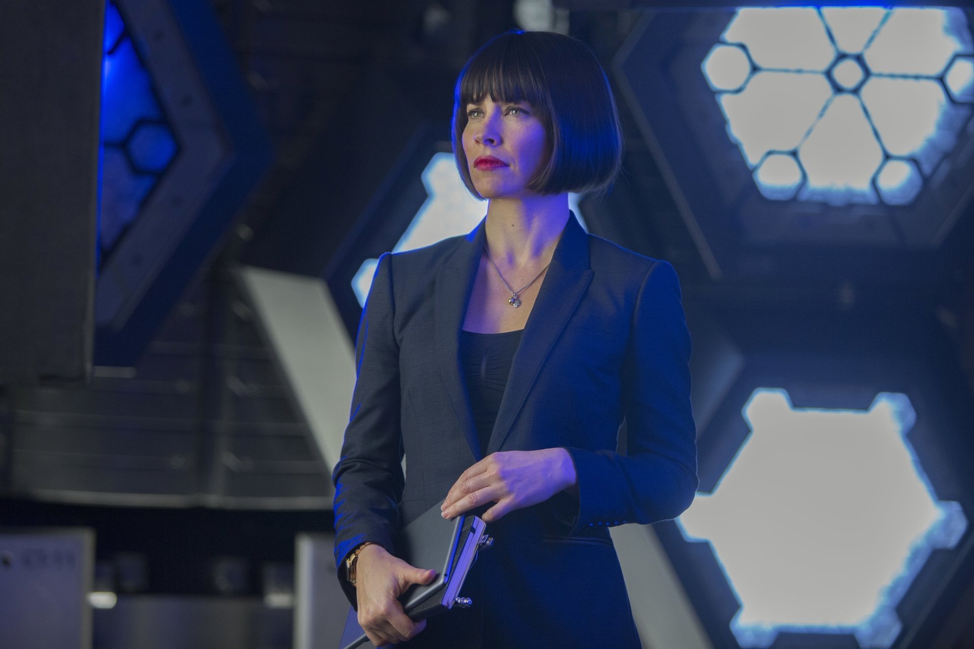 Woman in a black suit holding a device in a hex-lit high-tech lab — cinematic Ant-Man movie scene, 5K Ultra HD PC desktop wallpaper.