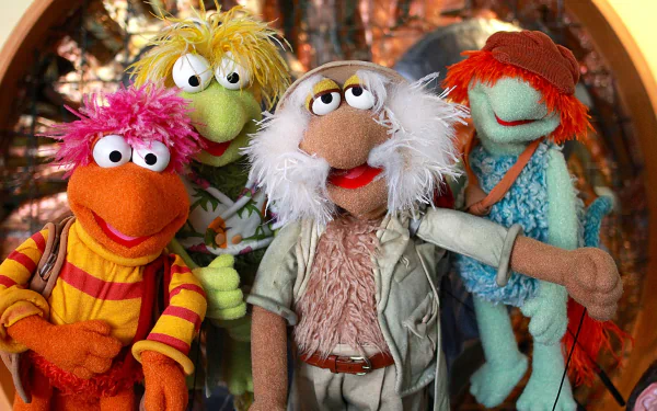 HD PC desktop wallpaper: The Muppets' Fraggle Rock characters — four colorful Fraggles smiling together in front of a glowing cave tunnel background.