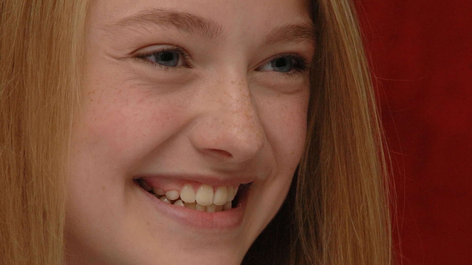 Close-up HD PC desktop wallpaper of celebrity Dakota Fanning smiling against a red background.