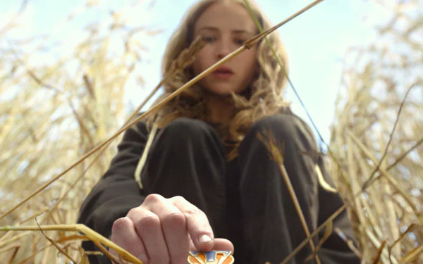 Brittany Robertson from the movie Tomorrowland sits in a field, reaching toward a small orange and white object, captured in this HD PC desktop wallpaper.