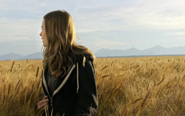HD desktop wallpaper featuring Brittany Robertson from the movie Tomorrowland, standing in a golden wheat field with mountains in the background.