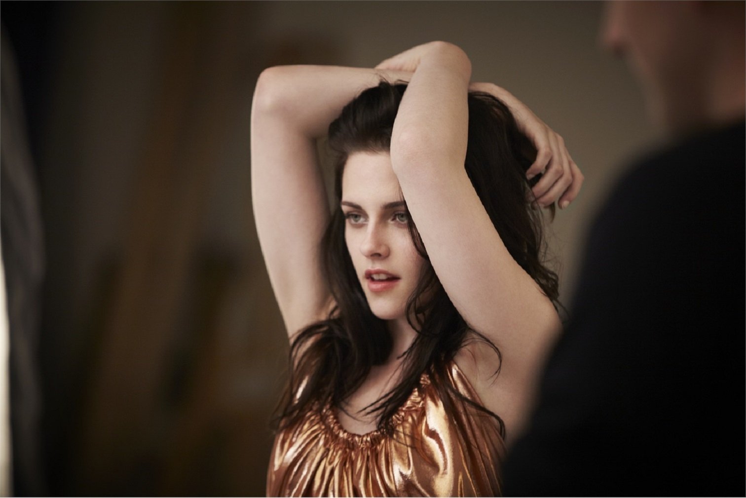 HD desktop wallpaper featuring celebrity Kristen Stewart with arms raised, wearing a shimmering top, and gazing into the distance.