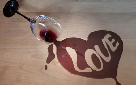Artistic HD wallpaper featuring a spilled glass of wine forming a heart shape with LOVE written inside on a wooden background.